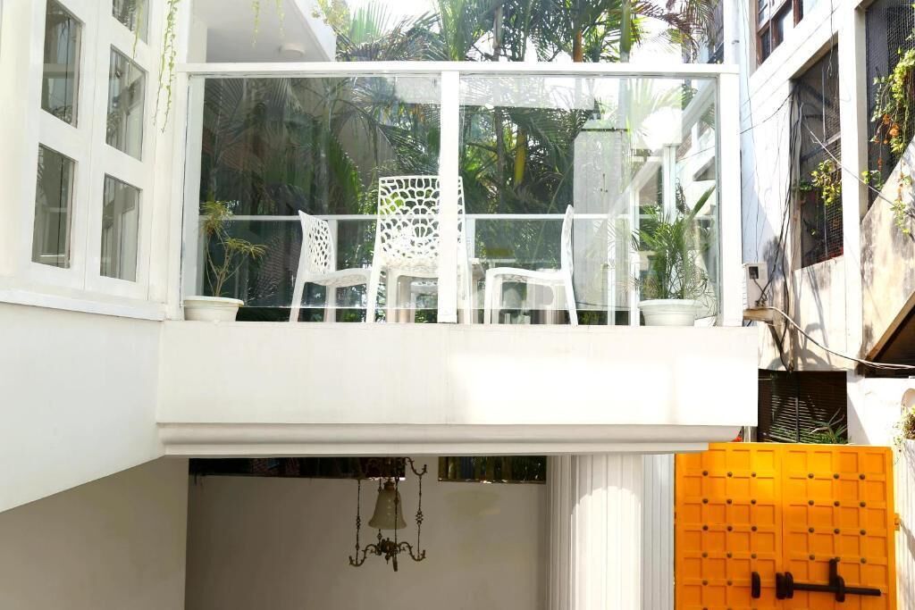 A balcony with white chairs and a glass railing overlooking a garden.