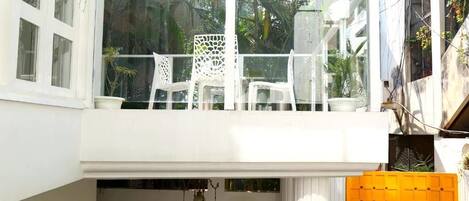 A balcony with white chairs and a glass railing overlooking a garden.