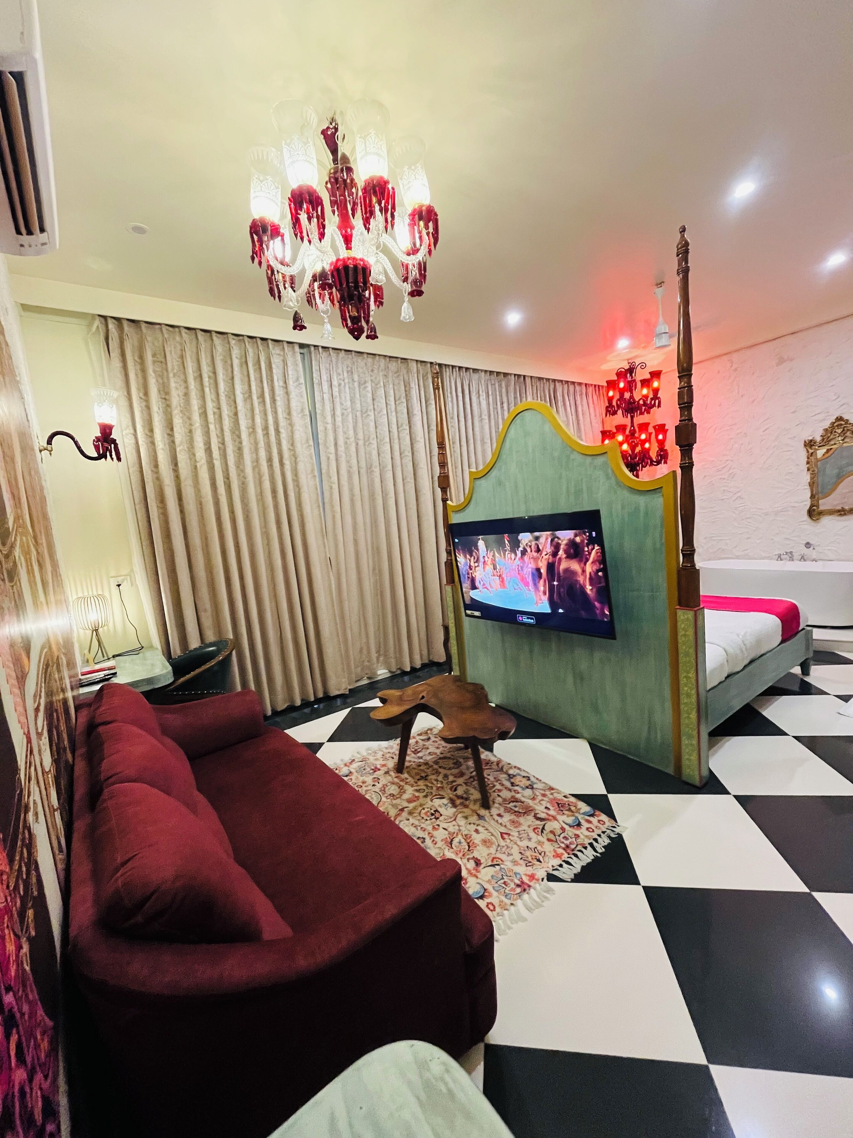 A modern living room with a large flat-screen TV, a red sofa, a patterned rug, and a chandelier.