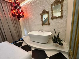 A bathroom with a freestanding bathtub, two wall-mounted mirrors, and a chandelier.