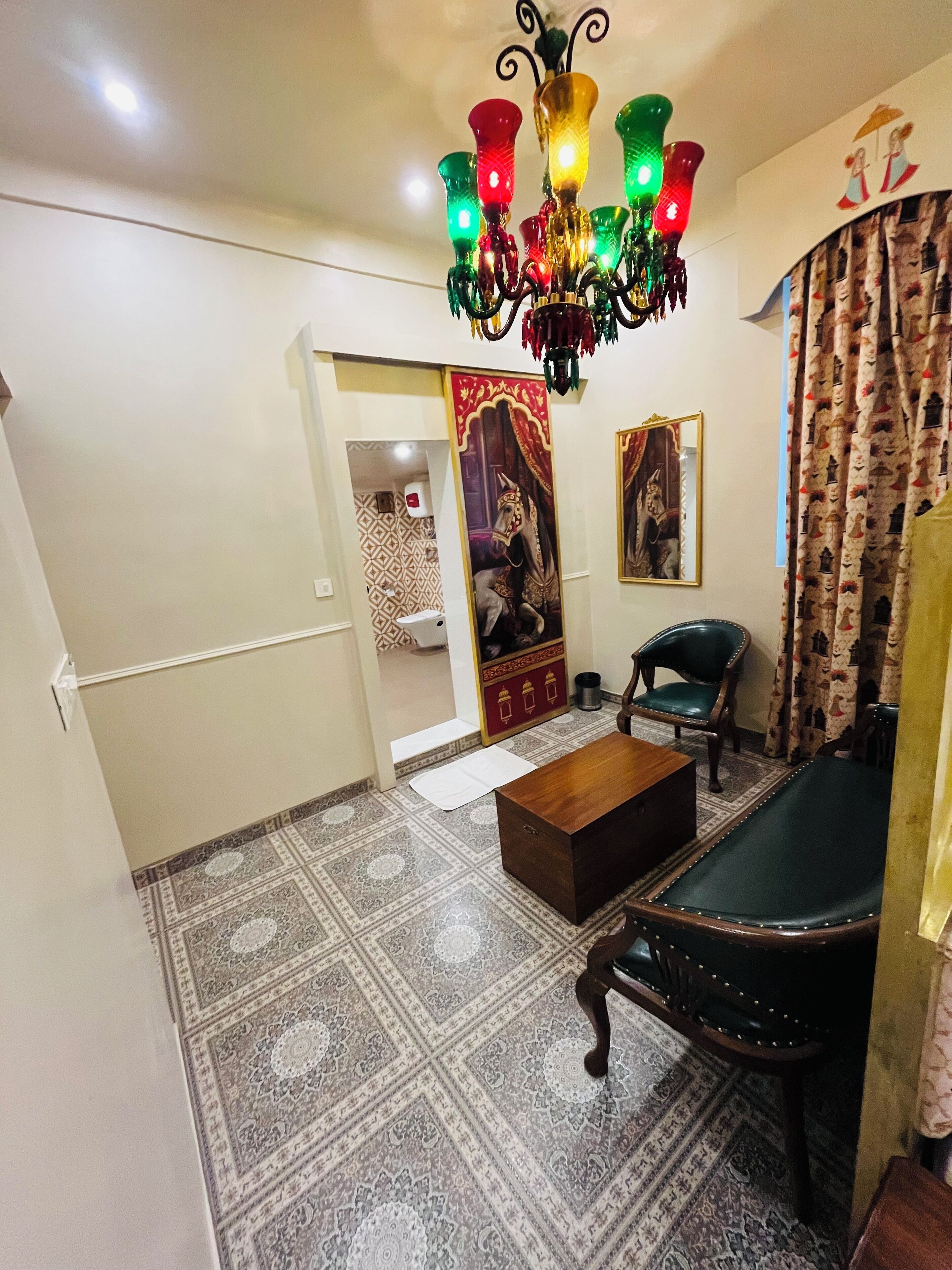 A living room with a patterned carpet, a wooden coffee table, a green armchair, a black leather sofa, a chandelier, and a door leading to another room.