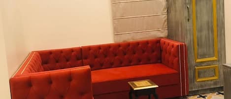 Un sofá rojo, un taburete pequeño, un suelo estampado, un aire acondicionado instalado en la pared y un armario de madera con detalles dorados.
