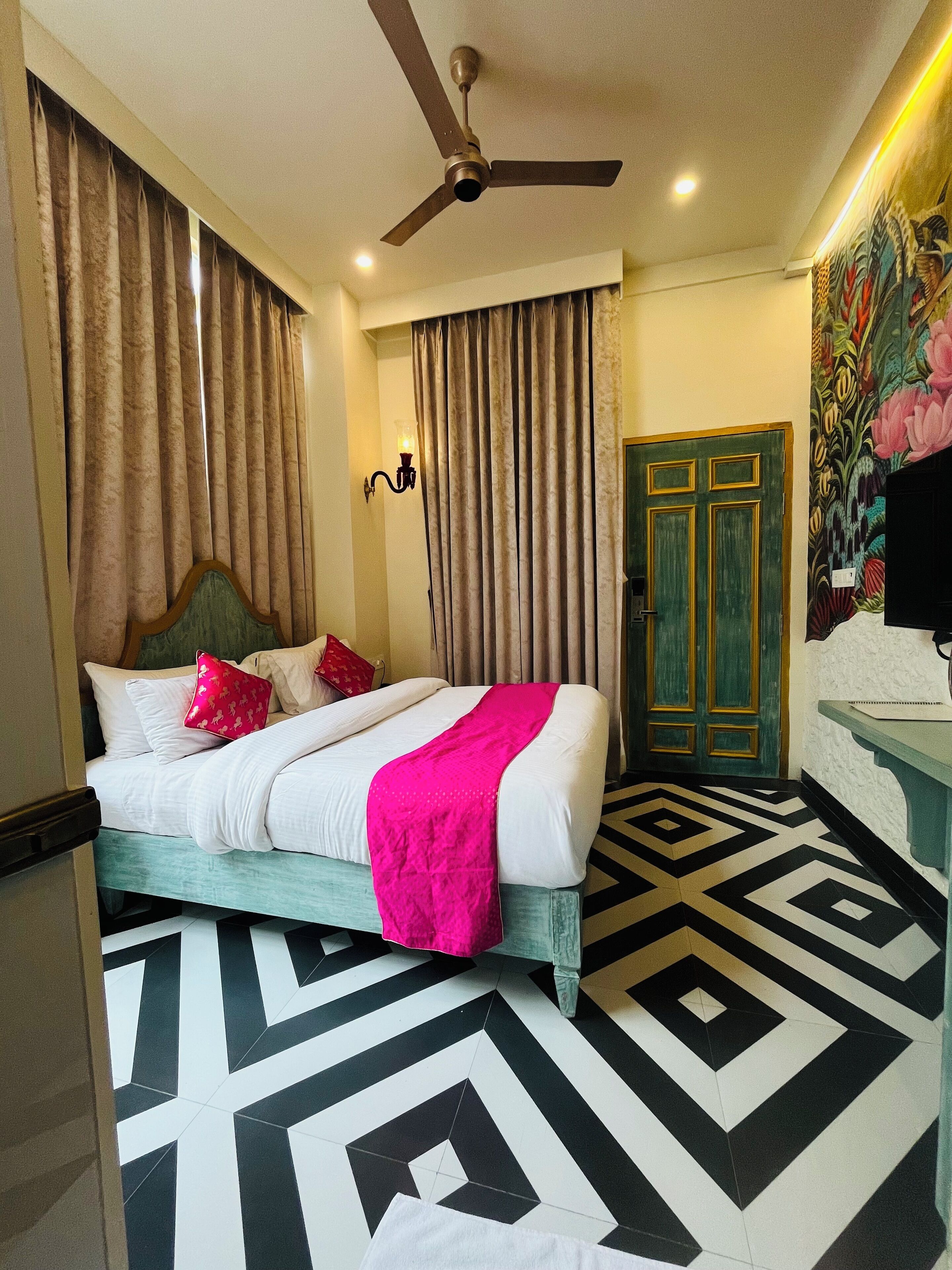 A hotel room with a bed, curtains, a ceiling fan, a door, and a patterned floor.