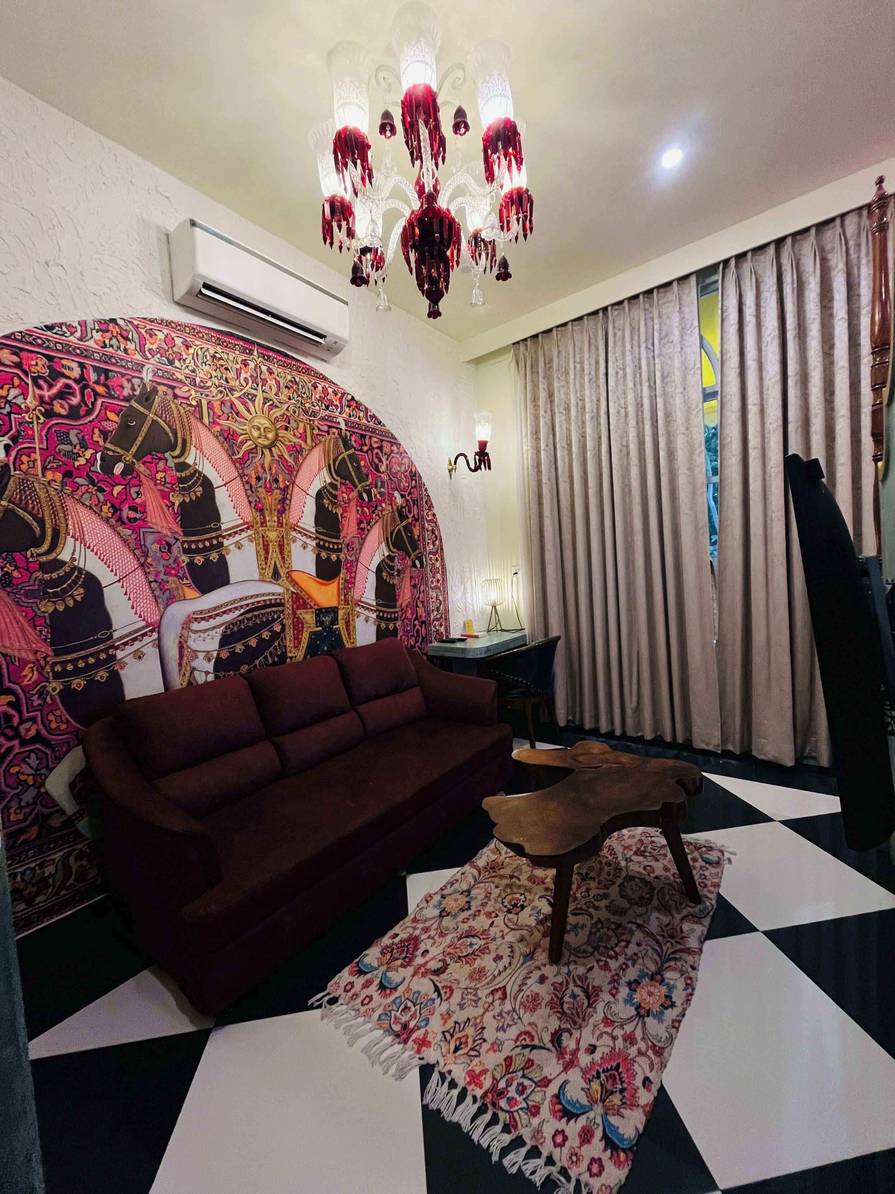 A living room with a red sofa, a patterned rug, a chandelier, and a large tapestry.
