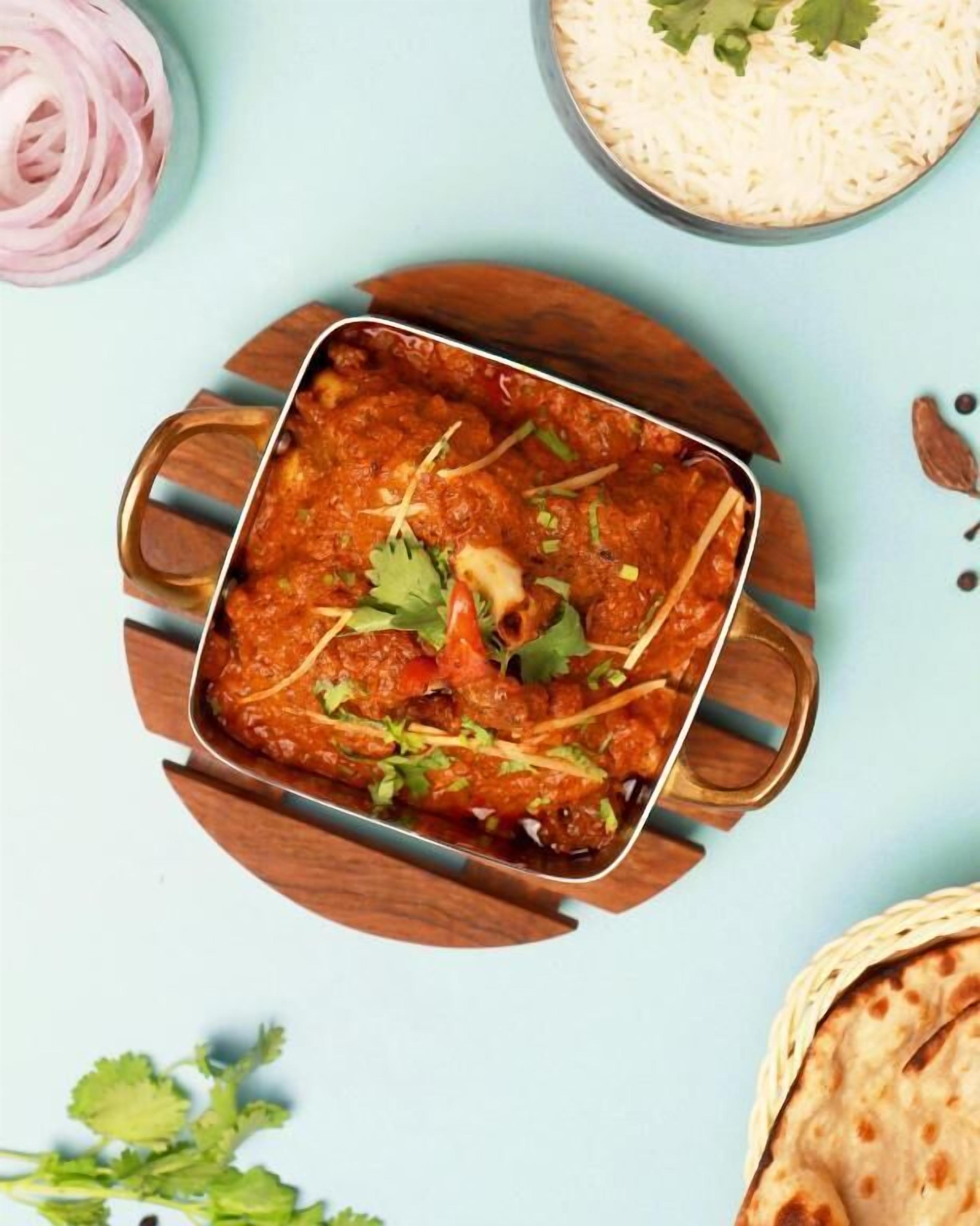 Un plat de poulet tikka masala servi dans un plat en métal, posé sur une planche en bois.