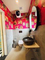 A bathroom with a red patterned wall, a white toilet, a black sink, and a mirror.