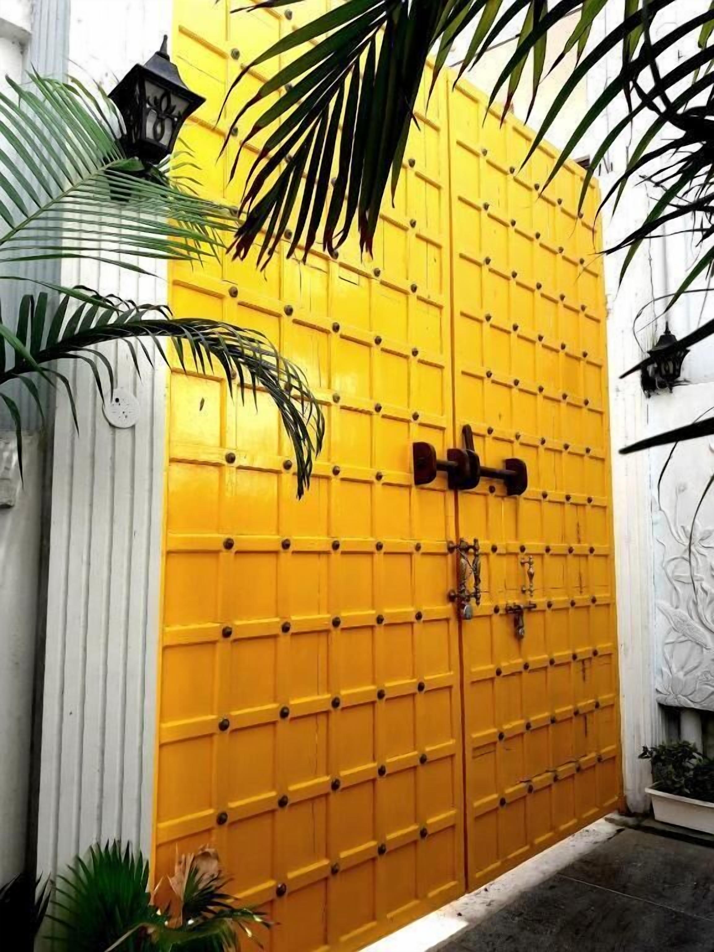 A yellow gate with a lock and a keyhole, surrounded by plants and a white wall.