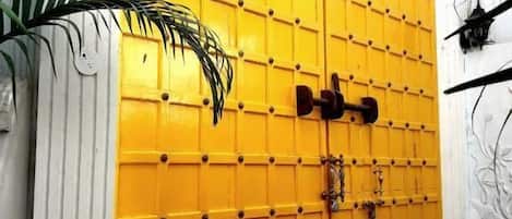 A yellow gate with a lock and a keyhole, surrounded by plants and a white wall.