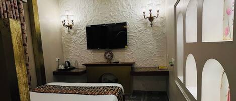 A hotel room with a bed, a desk, a television, a clock, and a patterned rug.
