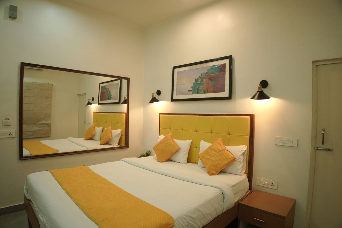 A hotel room with a bed, a nightstand, a mirror, a wall-mounted picture, and a door.
