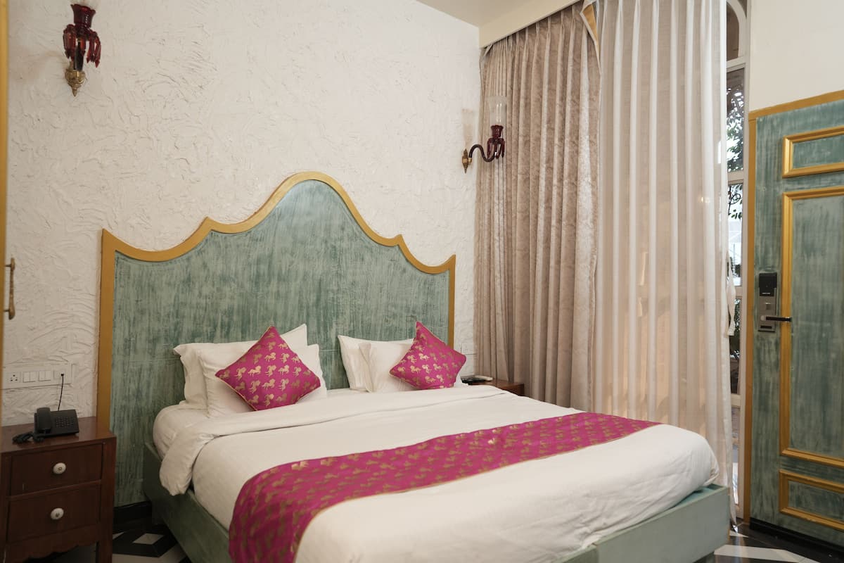 A hotel room with a bed, a nightstand, a lamp, and a door.
