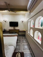 A hotel room with a bed, a desk, a flat-screen TV, a chandelier, and decorative wall mirrors.