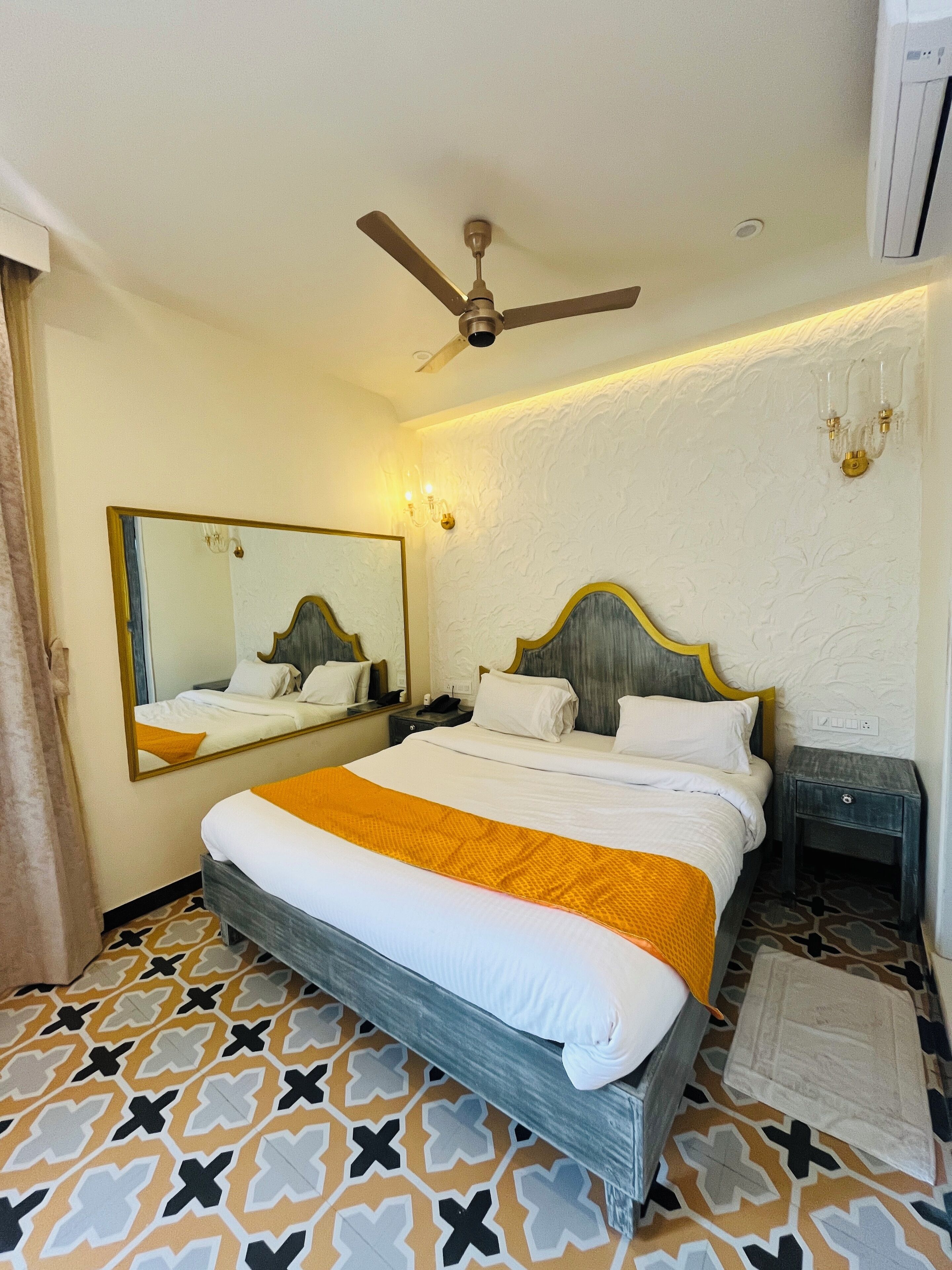 A hotel room with a bed, a ceiling fan, a mirror, and a patterned floor.