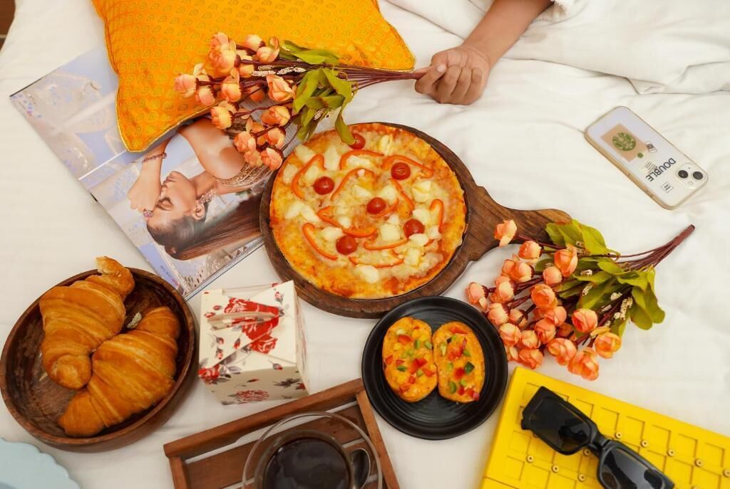 Desayuno con cruasanes, una pizza y un ramo de flores sobre una cama.