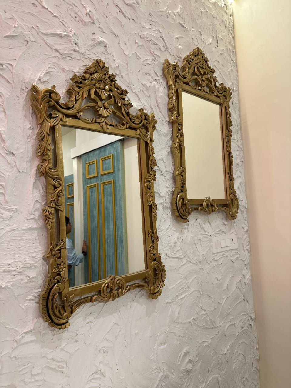 Dos espejos ornamentados con marcos dorados sobre una pared blanca con textura.