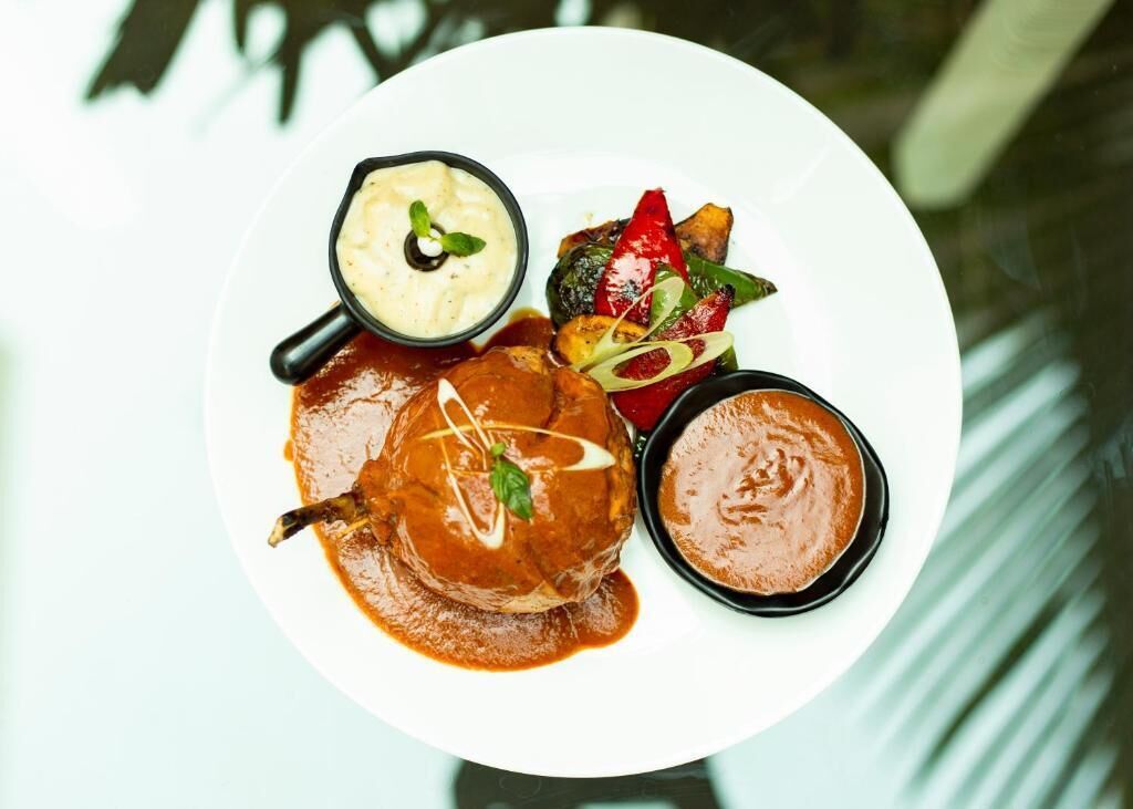 A plate with a meat dish, a bowl of sauce, and a small bowl of sauce.