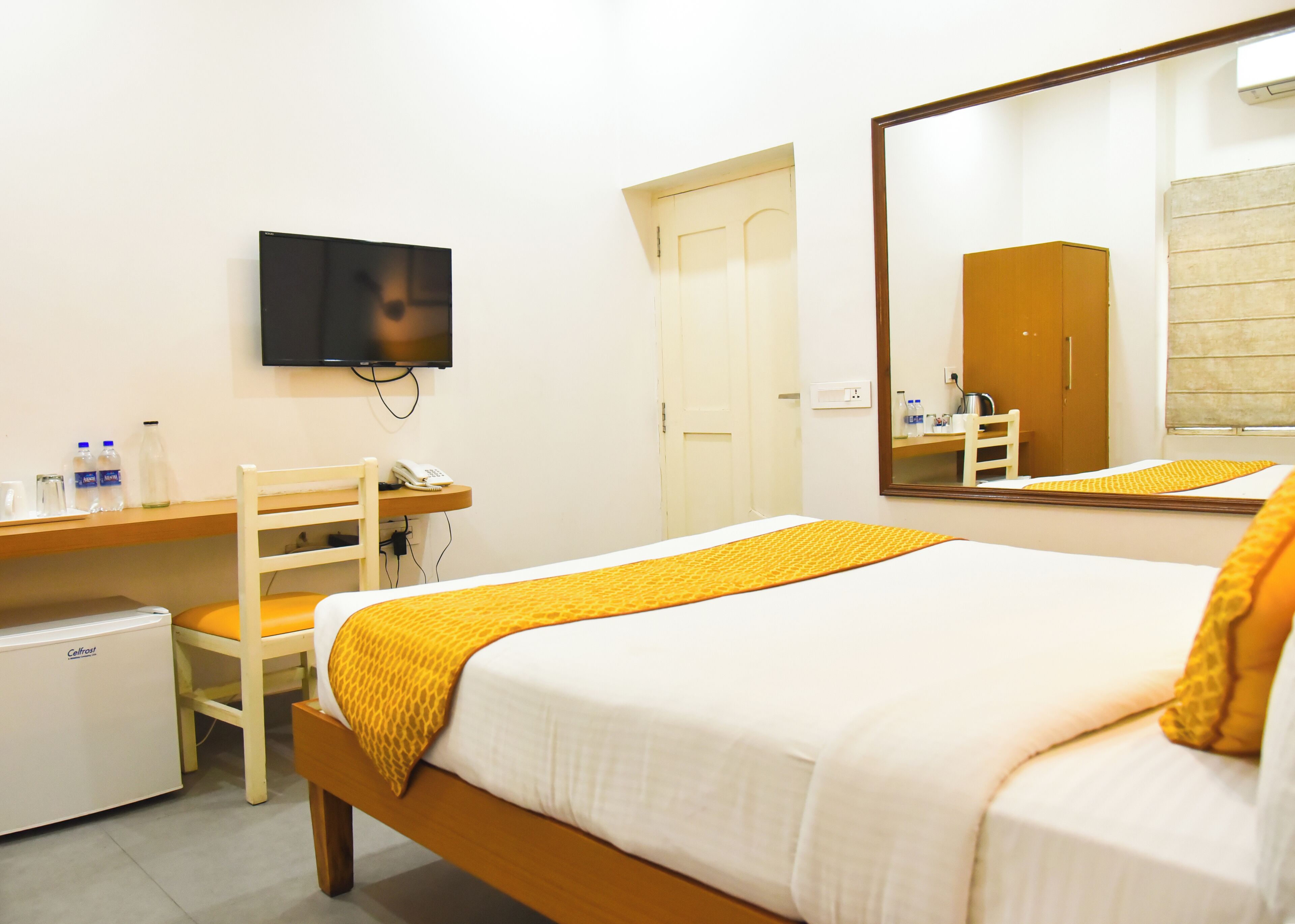 Een hotelkamer met een bed, een bureau, een stoel, een televisie, een kledingkast en een kleine koelkast.