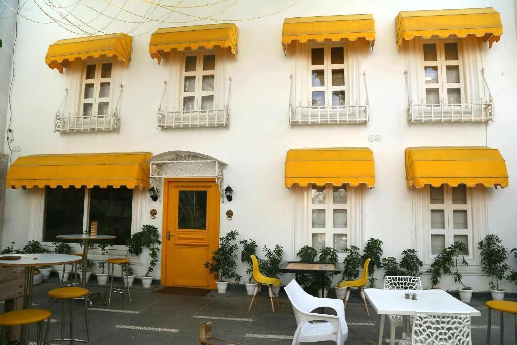 Un bâtiment doté de nombreuses fenêtres, dont certaines sont surmontées d’auvents jaunes, et de plusieurs tables et chaises placées à l’extérieur.