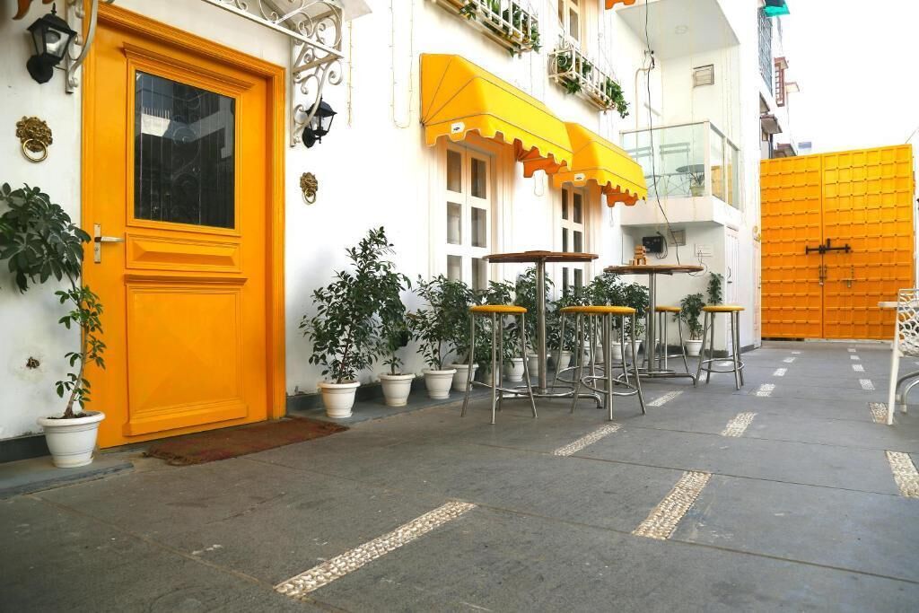 A narrow street with a yellow door and a yellow awning. There are potted plants and outdoor seating.
