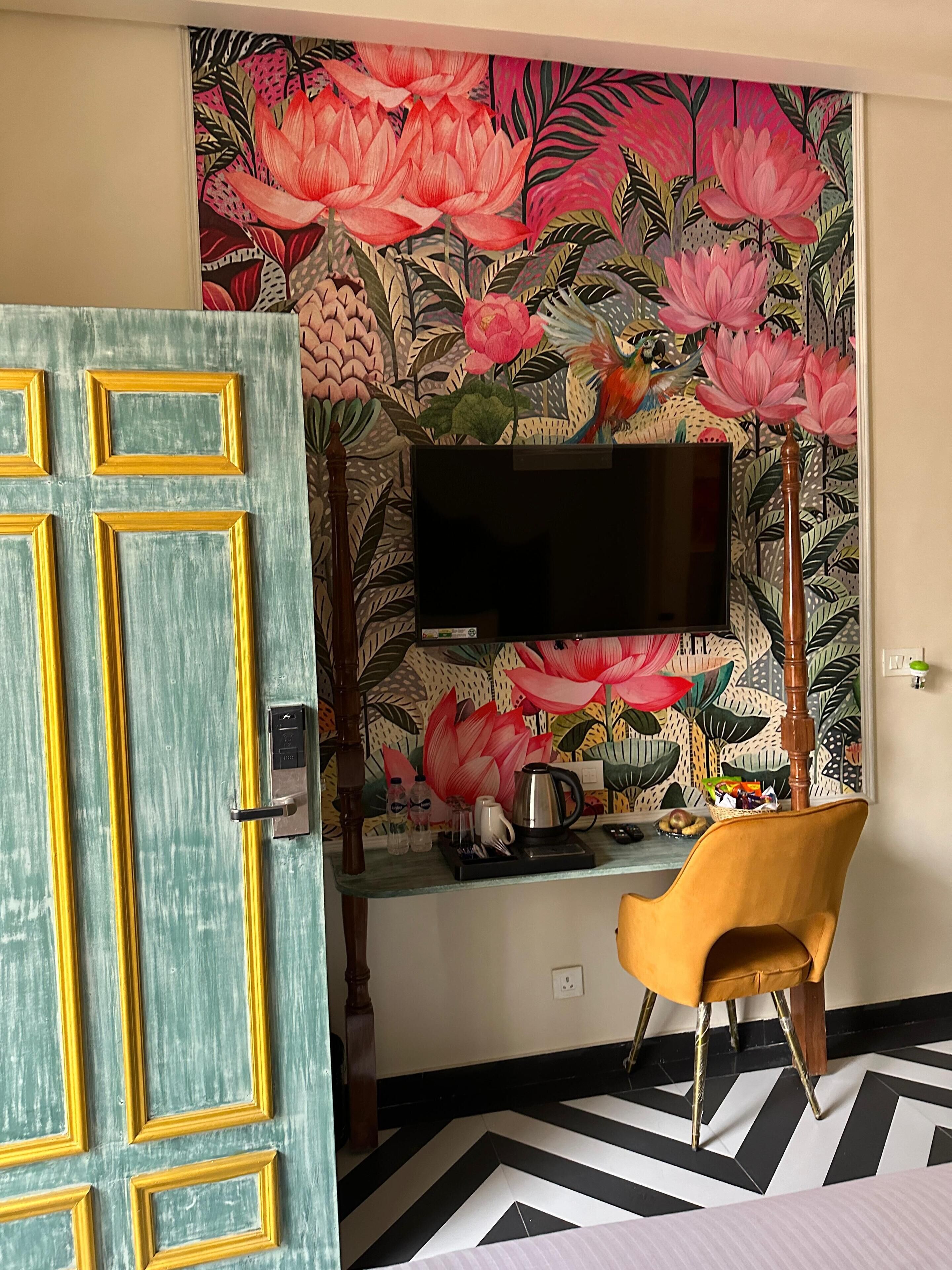 A room with a teal door, a flat-screen TV mounted on a wall with a floral mural, a yellow chair, and a black and white patterned floor.