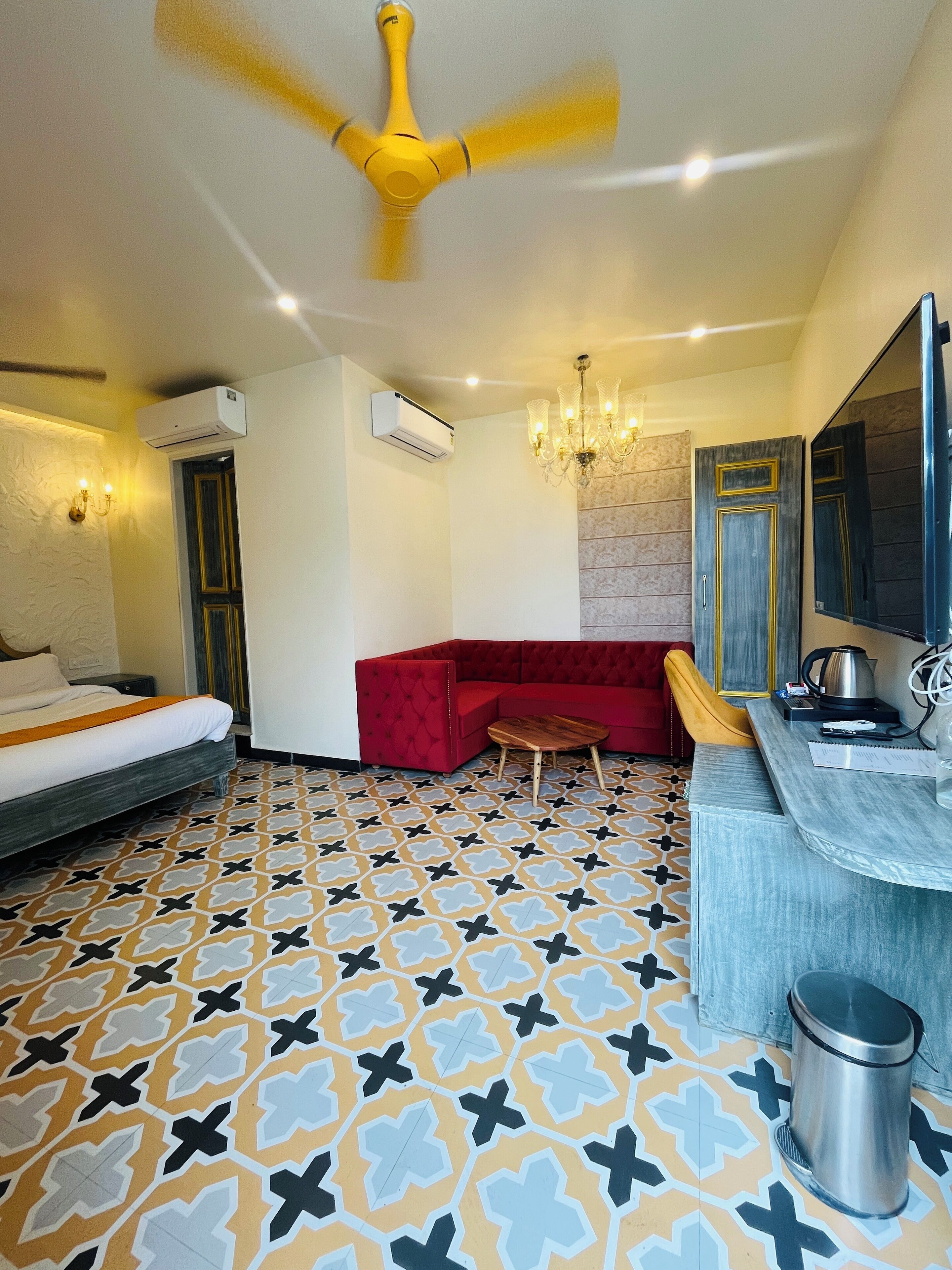 A hotel room with a bed, a red sofa, a small table, a mirror, and a ceiling fan.