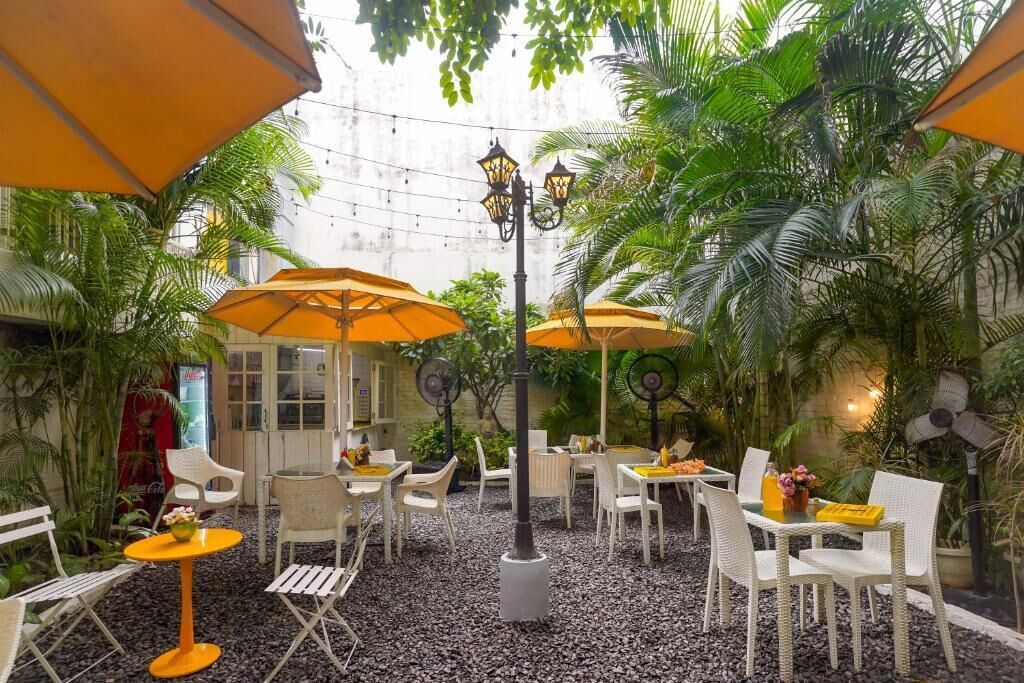 An outdoor café with tables and chairs, surrounded by greenery and umbrellas.