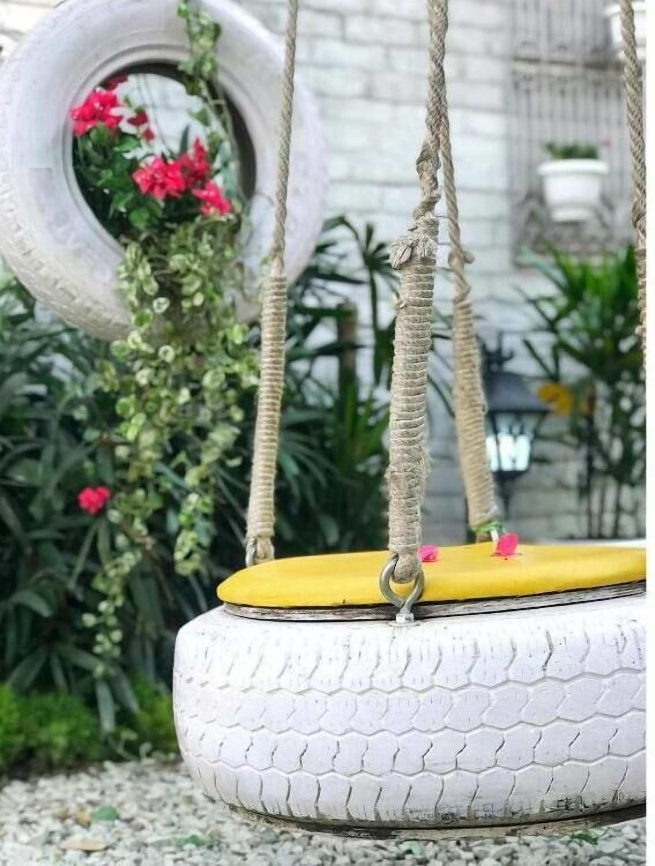 A tire swing with a yellow seat, ropes, and a tire wheel in the background.