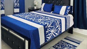 A bedroom with a bed, curtains, a nightstand, a potted plant, and a ceiling light fixture.
