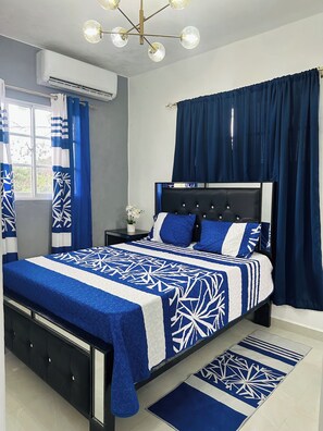 A bedroom with a bed, curtains, a nightstand, a potted plant, and a ceiling light fixture.