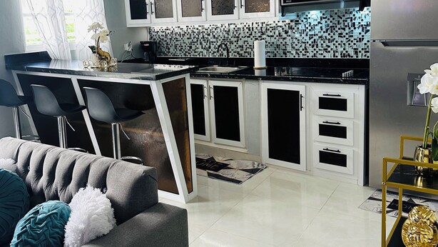 A modern kitchen with white cabinets, a black countertop, and a stainless steel refrigerator.