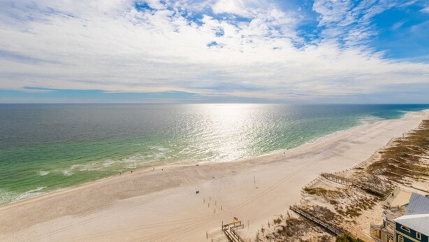 A beach with a clear sky, a sandy shore, and a few buildings in the background.