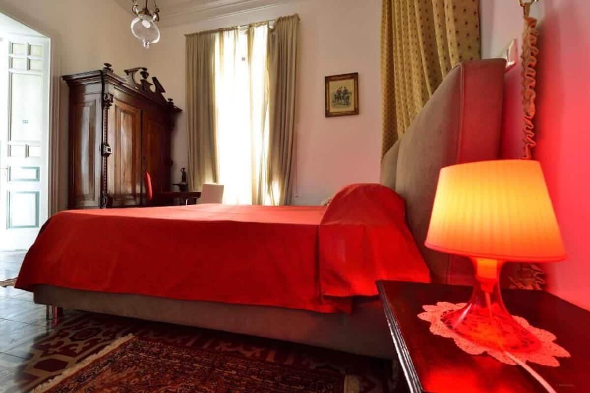 Un dormitorio con una cama, una mesita de noche, una lámpara, un armario y una ventana con cortinas.