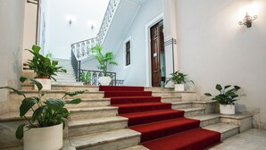 Una imponente escalera con peldaños de mármol y alfombra roja, que conduce a un balcón con barandilla de metal.
