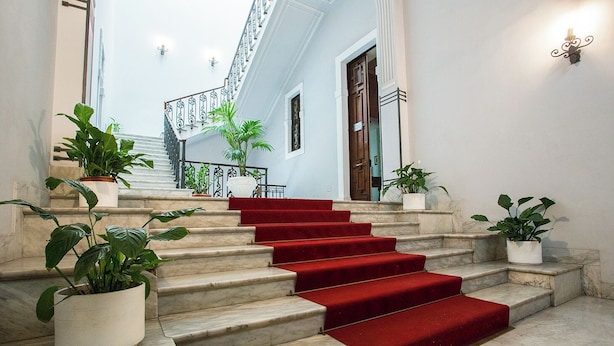 Una imponente escalera con peldaños de mármol y alfombra roja, que conduce a un balcón con barandilla de metal.