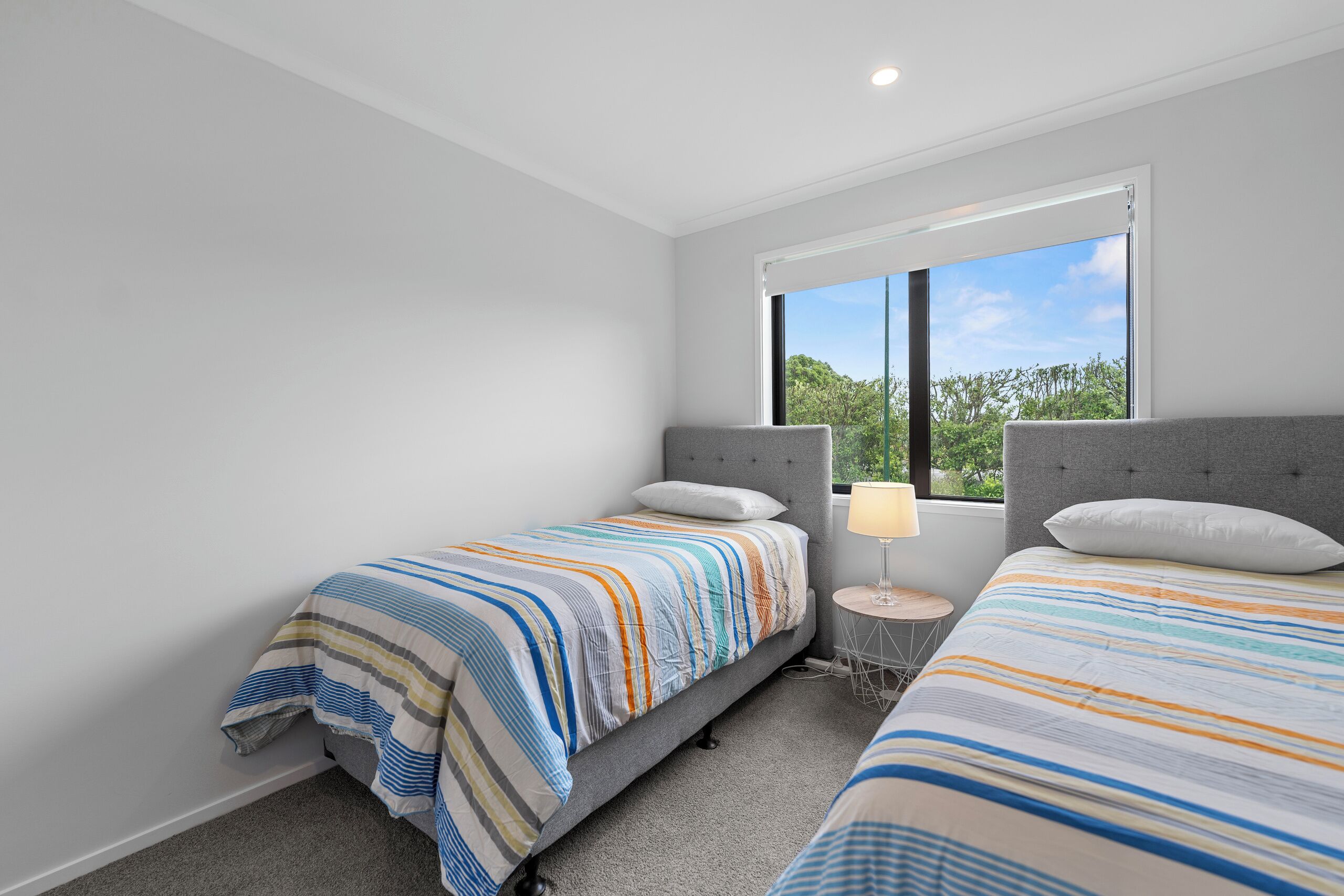 Une chambre moderne avec deux lits, une fenêtre donnant sur un paysage verdoyant et une petite table ronde avec une lampe.
