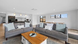 Ein modernes Wohnzimmer mit zwei grauen Sofas, einem Holztisch und einer Küche im Hintergrund.