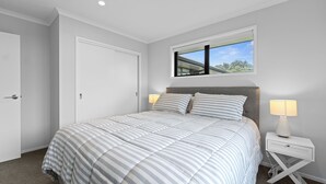 Ein Schlafzimmer mit einem großen Bett, einem Nachttisch mit Lampe, einem Fenster mit Blick auf Grünflächen und einer Tür.