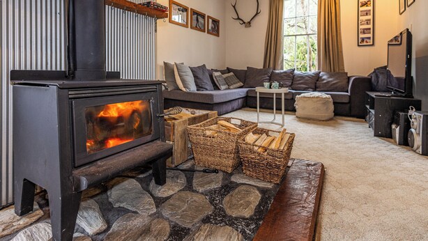 A cozy living room with a stone fireplace, a sofa, and a television. - Willow Lodge - Ohakune Holiday Home (Ohakune)