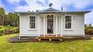 A white single-story house with a front porch, a satellite dish, and a small garden area. - Willow Lodge - Ohakune Holiday Home (Ohakune)