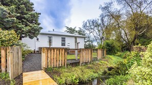 A wooden deck leading to a house with a gravel driveway and a small stream. - Willow Lodge - Ohakune Holiday Home (Ohakune)