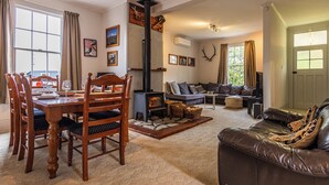 A cozy living room with a fireplace, a dining area with wooden chairs, and a leather sofa. - Willow Lodge - Ohakune Holiday Home (Ohakune)