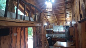 A rustic wooden cabin interior with a kitchen area, wooden beams, and a hanging light fixture. - Cabañas Rucapillan (Panguipulli)