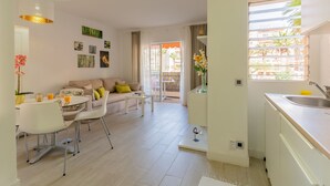 Ein modernes Wohnzimmer mit Sofa, Couchtisch und Essbereich. Es gibt eine Küche mit Spüle und einem Fenster mit Blick auf Gebäude.