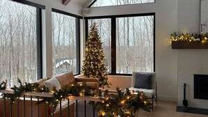 Un salon spacieux avec de grandes fenêtres, une cheminée et un sapin de Noël décoré.