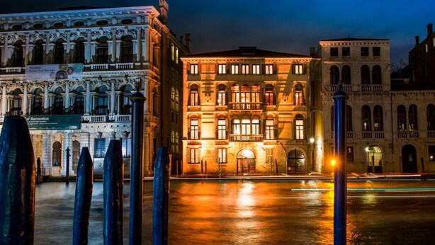 A historic building with classical architecture, a reflective water surface in front, and illuminated windows. - Monty Don's secret garden on the Grand Canal (Venezia)