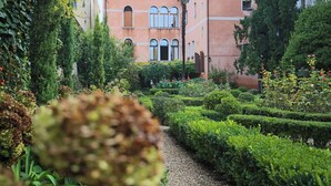 A garden pathway leading to a building with arched windows and a balcony. - Monty Don's secret garden on the Grand Canal (Venezia)