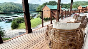 Une terrasse en bois, agrémentée de chaises en osier, qui offre une vue sur un lac et une montagne.