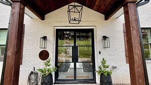 Une entrée moderne avec une pergola en bois, une porte noire et un paillasson.