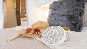 A bed with a white blanket, a straw hat, sunglasses, and a white woven basket. - Apartamentos Velas al Mar - by SOHO (Santa Marta)