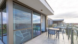 Ein modernes Gebäude mit großen Glasfenstern, einem Balkon mit Tisch und Stühlen und Blick auf die Umgebung.